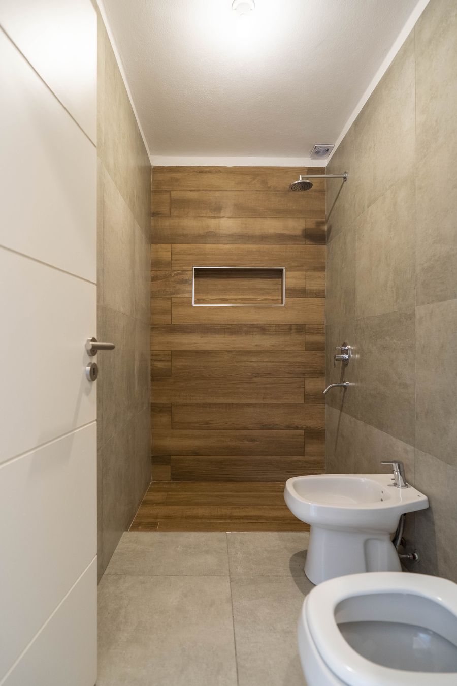 Baño con revestimiento símil madera en la ducha y porcelanato de gran formato