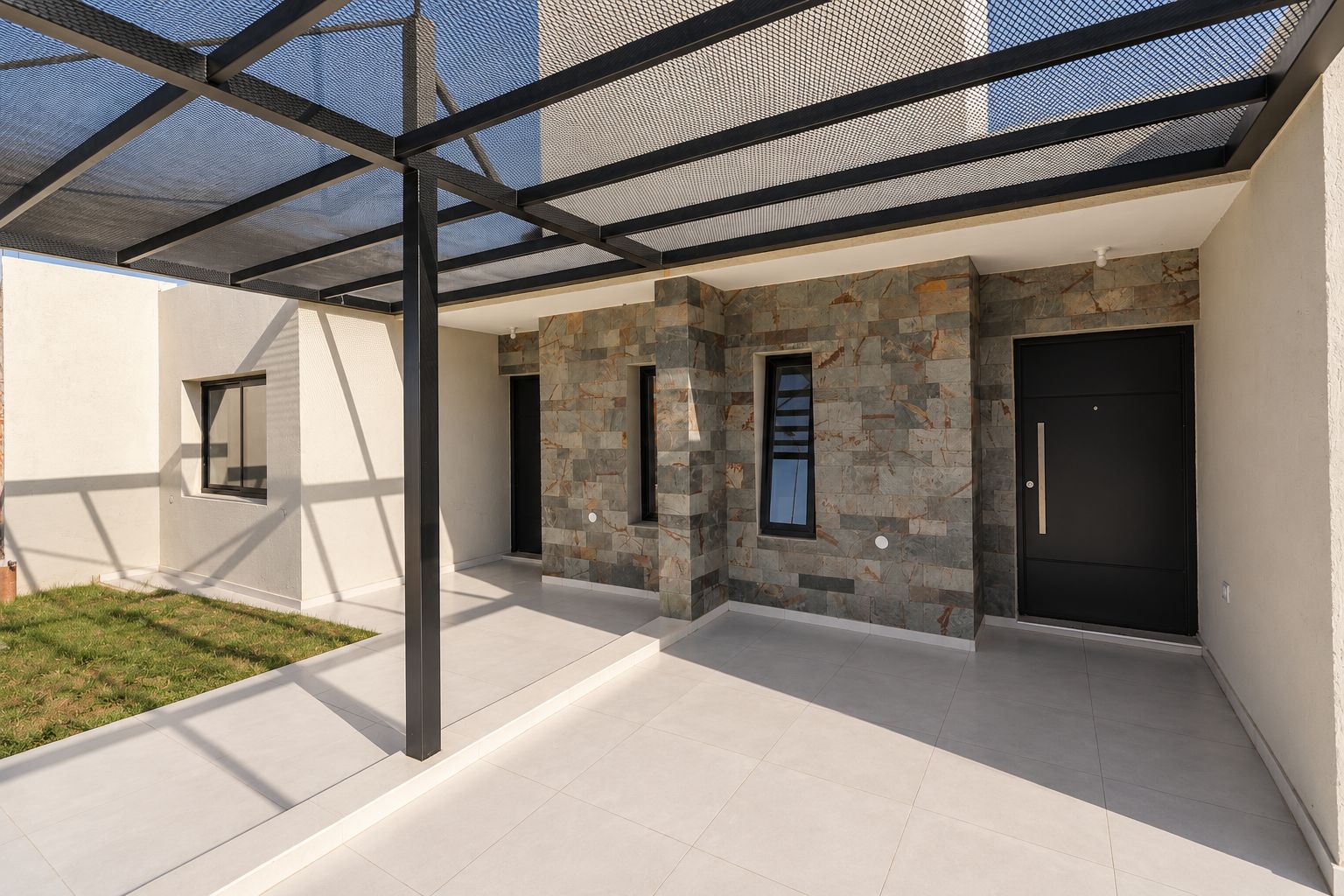 Acceso bajo la pérgola, con el revestimiento de piedra y las puertas de ingreso