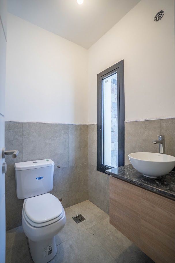 Toilette con bacha de apoyo sobre granito y ventana vertical